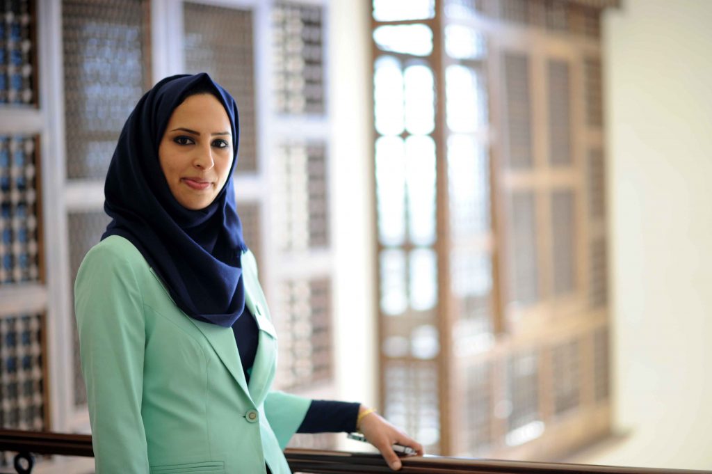 Alaa smiles at the camera in a light green blazer and navy headscarf.